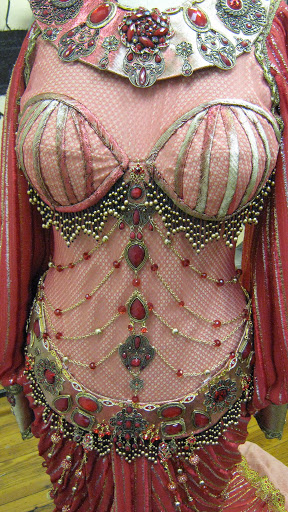 The dress features a boned bodice overlaid in red fishnet with beaded swags and operatic scale jewelry.